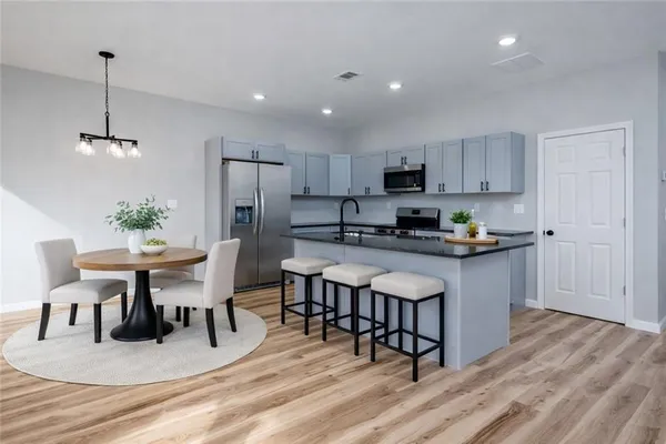 a kitchen with stainless steel appliances granite countertop a stove a refrigerator a microwave a dining table and chairs with wooden floor