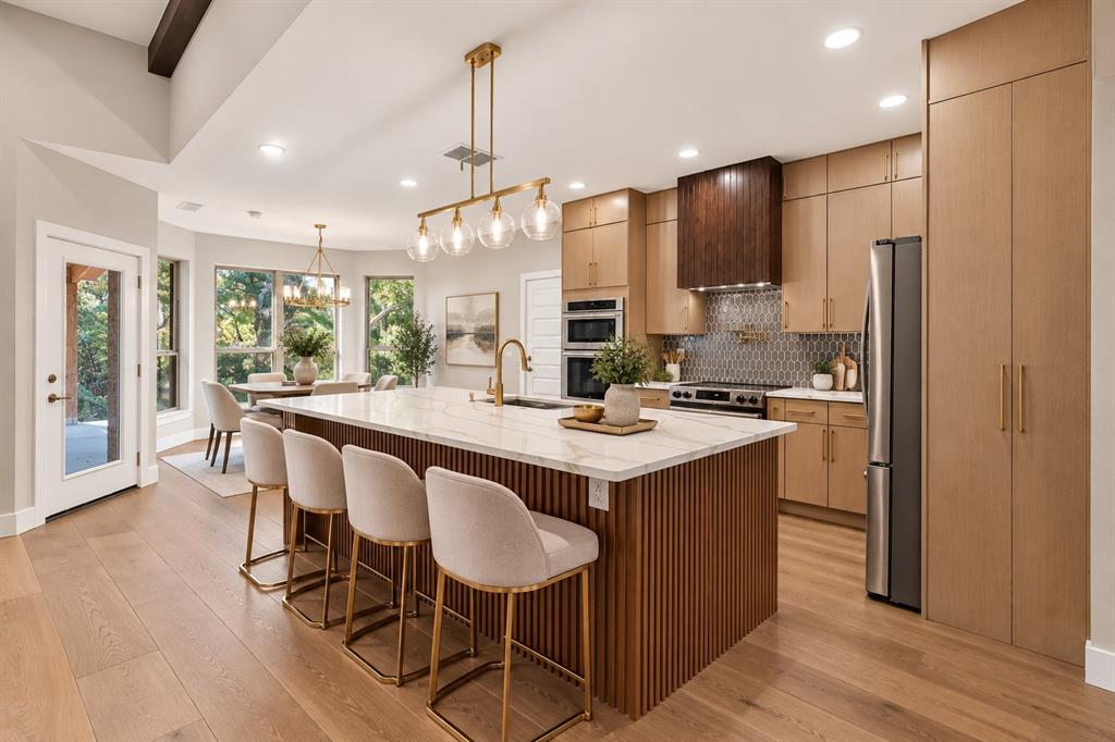 108 Winding Way Azle, TX 76020 - Photo 10 of 38 Virtually staged expansive kitchen featuring a large central island with a fluted wood base and light countertop, light wood-finish cabinetry, stainless steel appliances, and wood-finish flooring