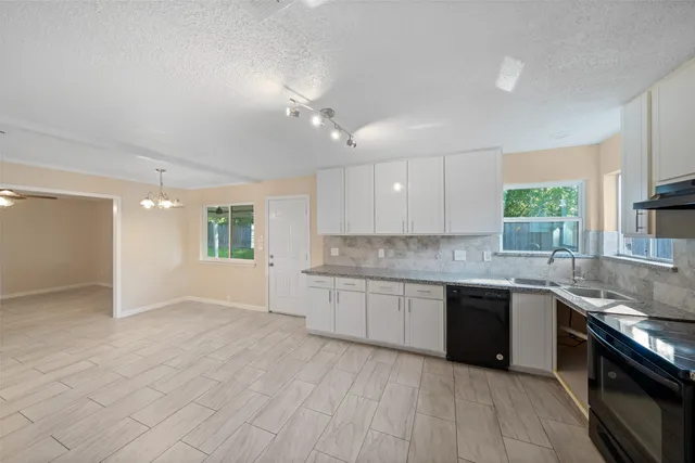 a large kitchen with granite countertop a stove top oven a sink dishwasher and white cabinets with wooden floor