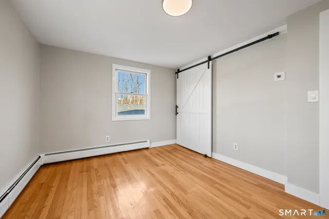 a view of an empty room with wooden floor and a window