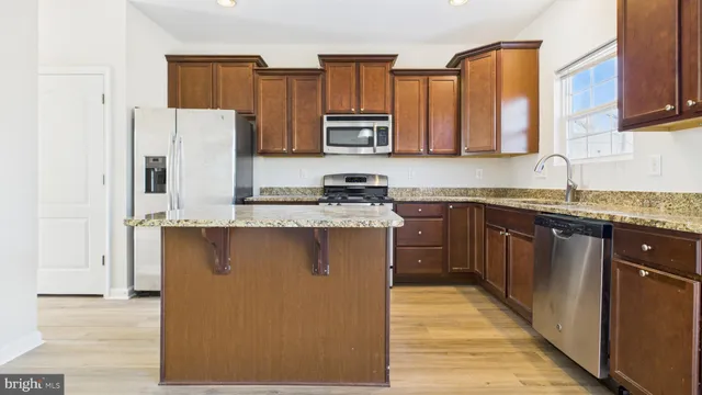 a kitchen with stainless steel appliances granite countertop a refrigerator a oven a sink dishwasher and white cabinets with wooden floor