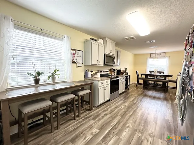 a kitchen with granite countertop a stove top oven a sink dishwasher and white cabinets with wooden floor