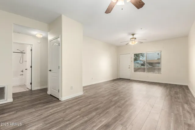 an empty room with wooden floor chandelier fan and windows