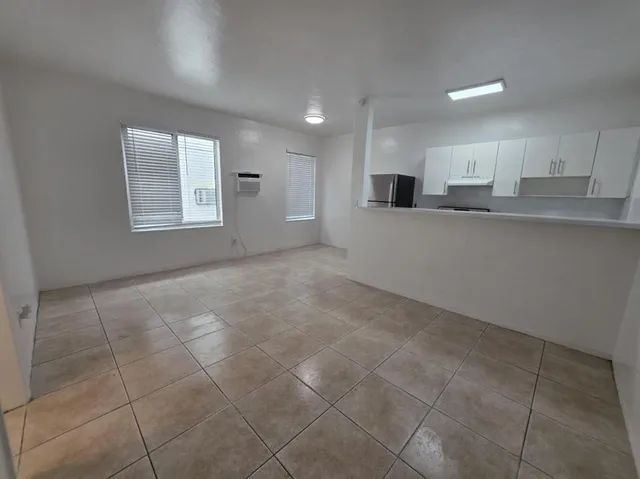 a view of an empty room with kitchen and window