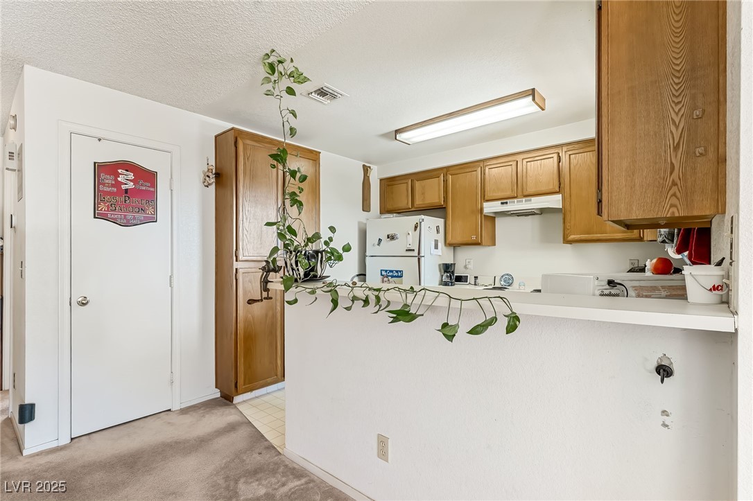 2180 Highpointe Drive, Unit 203 Laughlin, NV 89029 - Photo 5 of 20 Kitchen featuring freestanding refrigerator, brown cabinets, light countertops, light colored carpet, and a textured ceiling