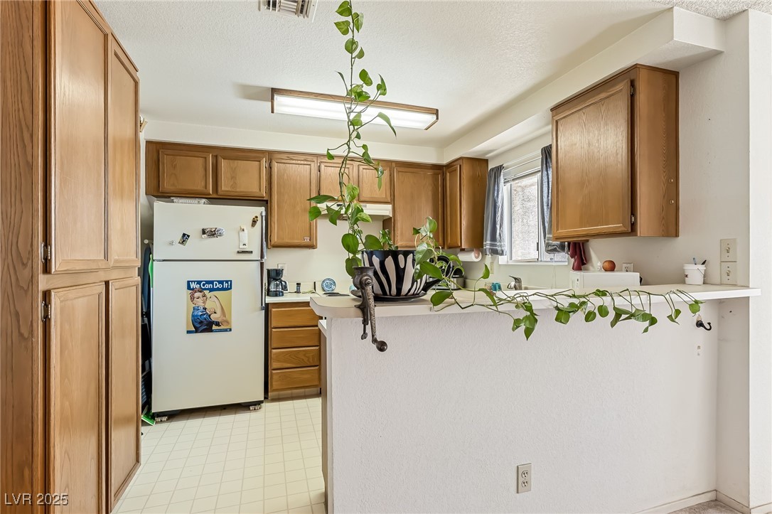 2180 Highpointe Drive, Unit 203 Laughlin, NV 89029 - Photo 6 of 20 Kitchen with freestanding refrigerator, a peninsula, light countertops, a textured ceiling, and brown cabinetry