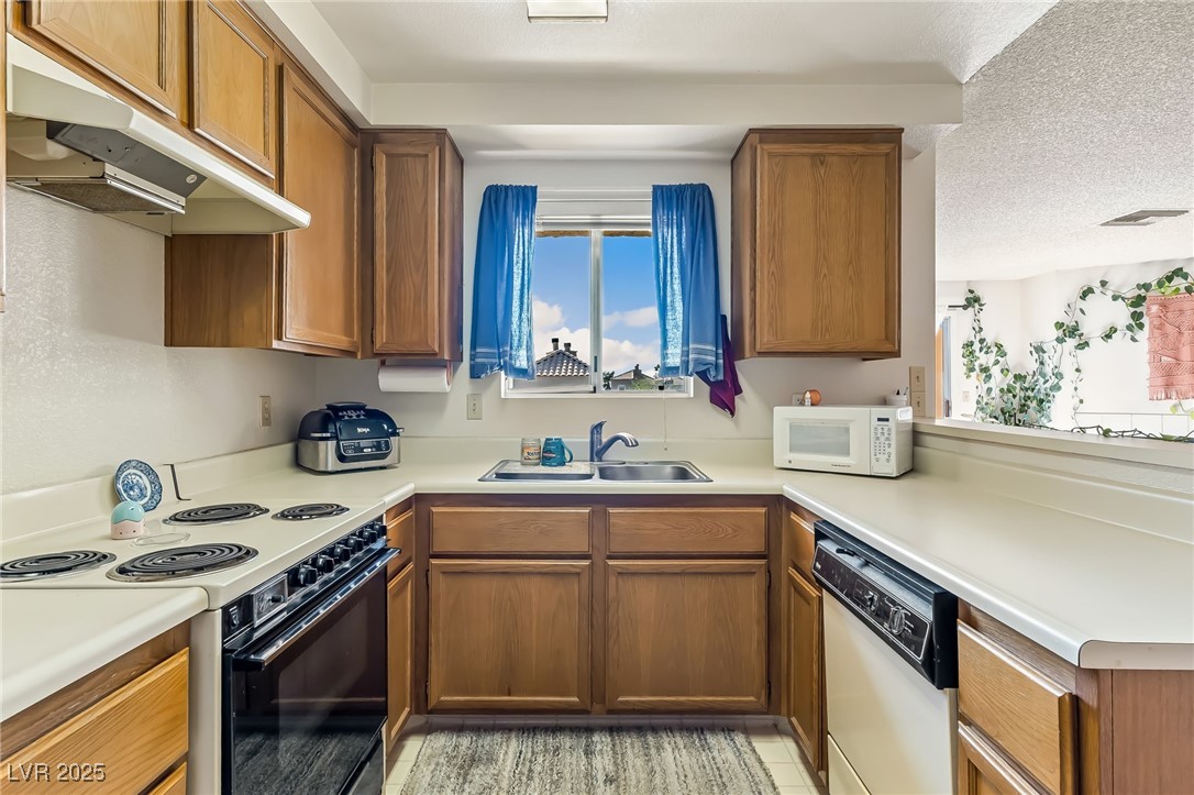 2180 Highpointe Drive, Unit 203 Laughlin, NV 89029 - Photo 7 of 20 Kitchen featuring white appliances, brown cabinetry, under cabinet range hood, a textured ceiling, and light countertops