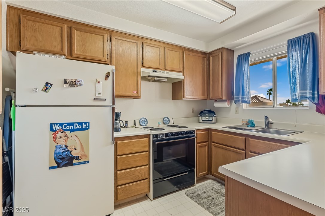 2180 Highpointe Drive, Unit 203 Laughlin, NV 89029 - Photo 9 of 20 Kitchen with freestanding refrigerator, black range with electric stovetop, light countertops, under cabinet range hood, and brown cabinetry