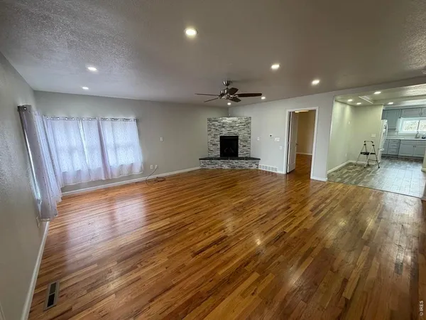 a view of an empty room with wooden floor and a kitchen