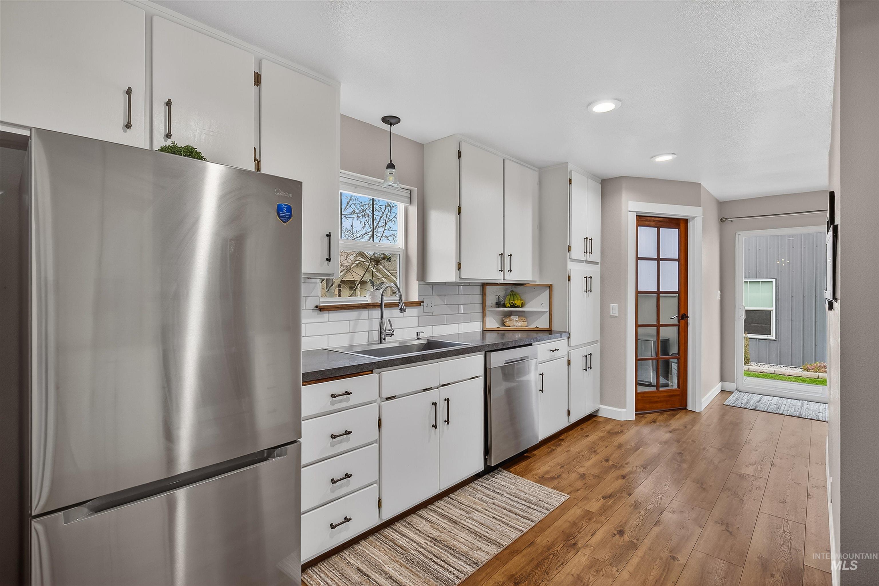 716 Chestnut Street Clarkston, WA 99403 - Photo 15 of 49 Kitchen featuring stainless steel appliances, dark countertops, white cabinetry, light wood-style floors, and backsplash