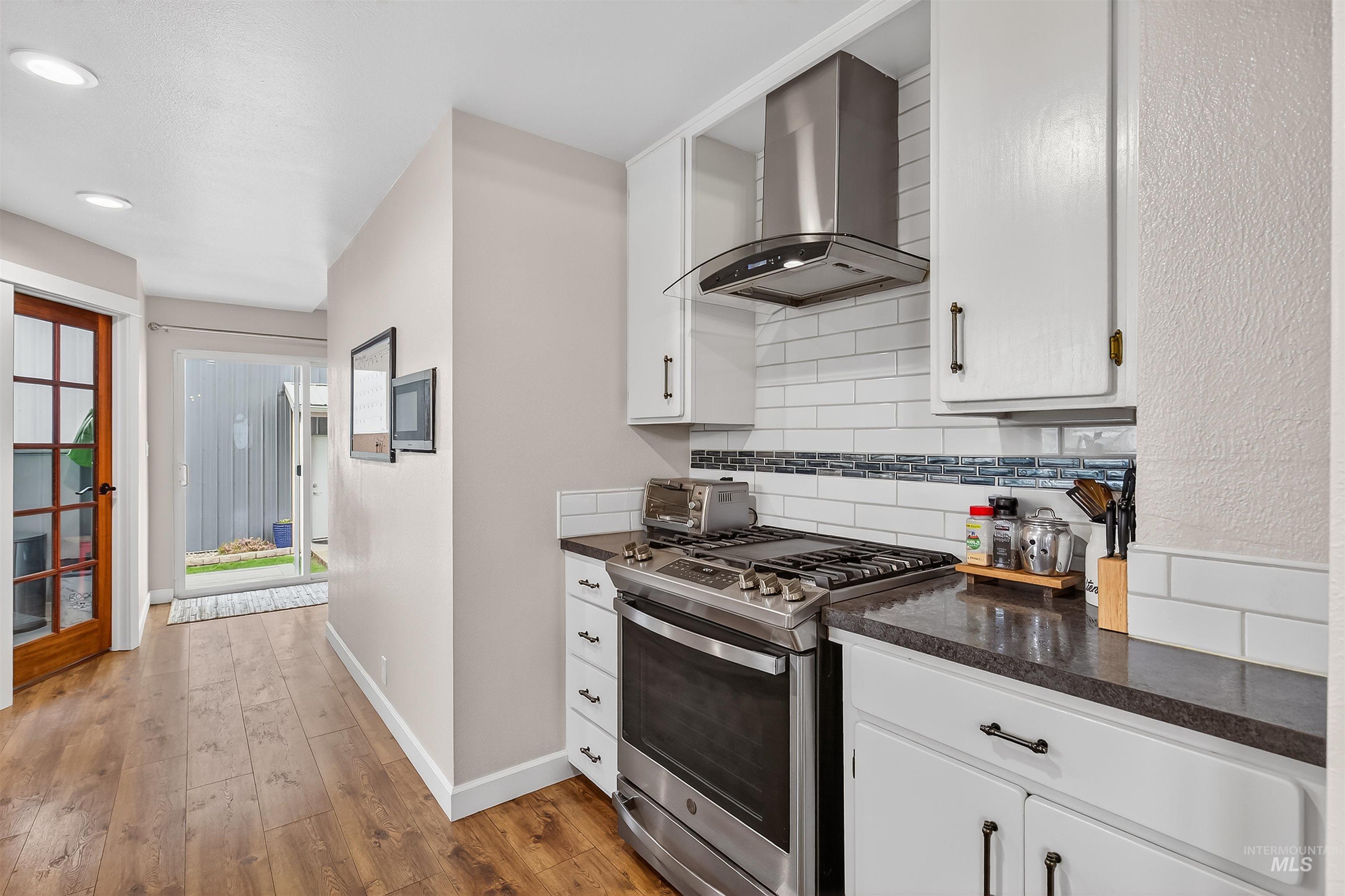 716 Chestnut Street Clarkston, WA 99403 - Photo 21 of 49 Kitchen with gas stove, extractor fan, white cabinetry, decorative backsplash, and light wood-type flooring