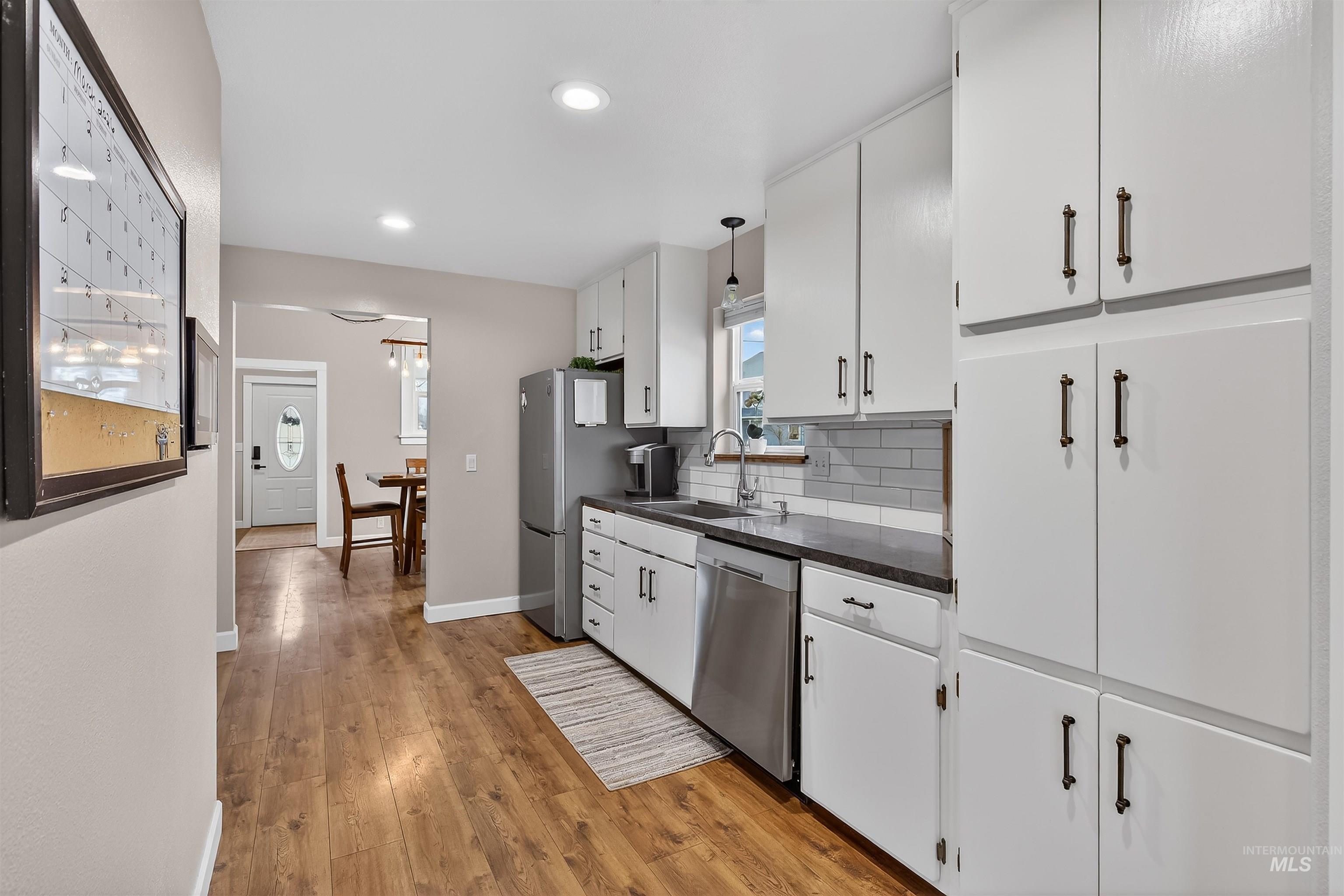716 Chestnut Street Clarkston, WA 99403 - Photo 22 of 49 Kitchen with dark countertops, light wood-style flooring, stainless steel appliances, white cabinetry, and decorative backsplash