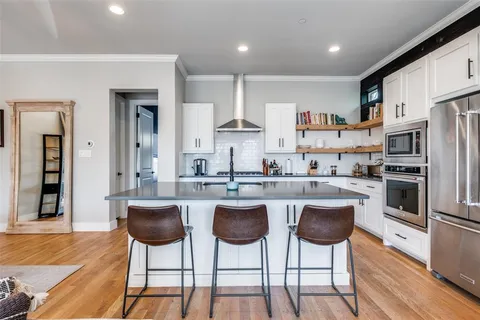 a kitchen with stainless steel appliances kitchen island granite countertop a stove a refrigerator and white cabinets with wooden floor