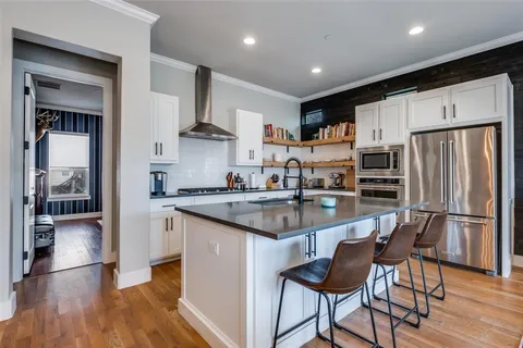 a kitchen with stainless steel appliances granite countertop a refrigerator a sink dishwasher a stove and white cabinets with wooden floor