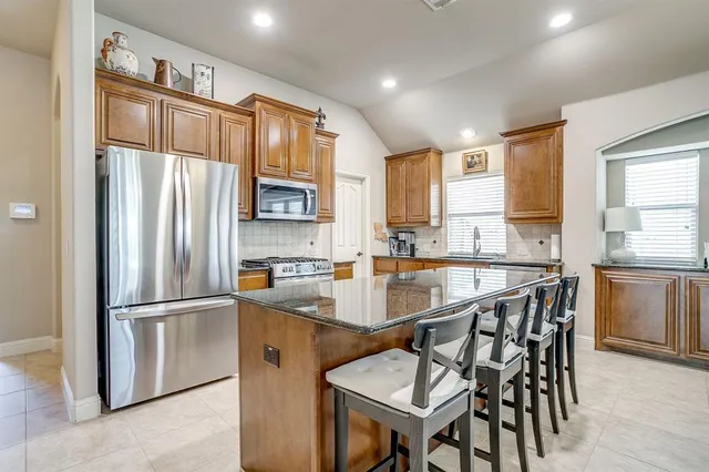 a kitchen with stainless steel appliances granite countertop a refrigerator a sink a stove a dining table and chairs