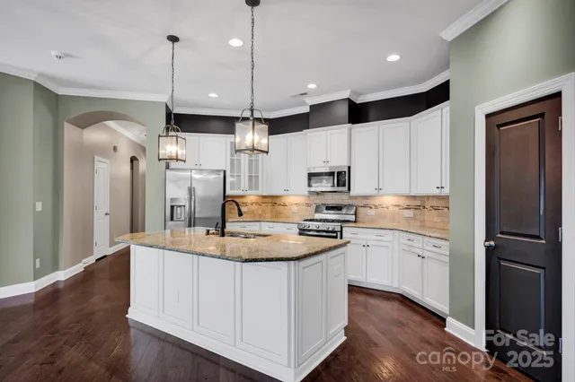 a kitchen with stainless steel appliances kitchen island granite countertop a refrigerator a sink dishwasher a stove and white cabinets with wooden floor