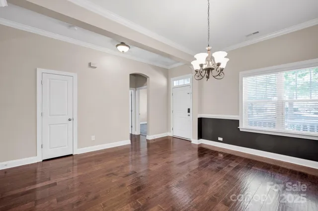 a view of an empty room with window chandelier and wooden floor