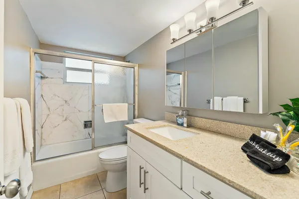 a bathroom with a granite countertop sink a toilet a mirror and shower