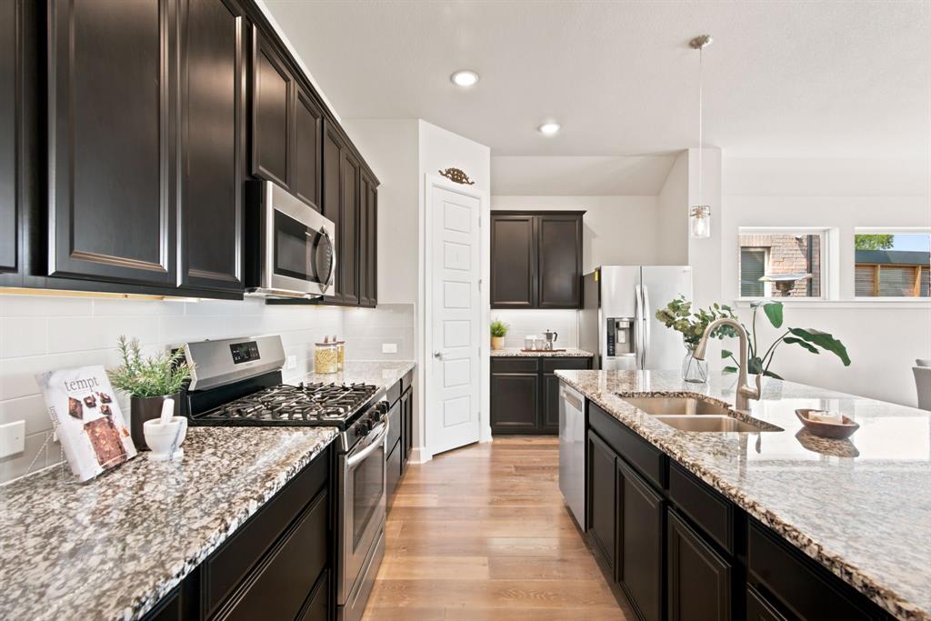 709 Bent Brook Road Oak Point, TX 75068 - Photo 10 of 27 Gourmet kitchen featuring dark wood cabinetry, granite countertops, stainless steel appliances, a tile backsplash, and wood-finish flooring