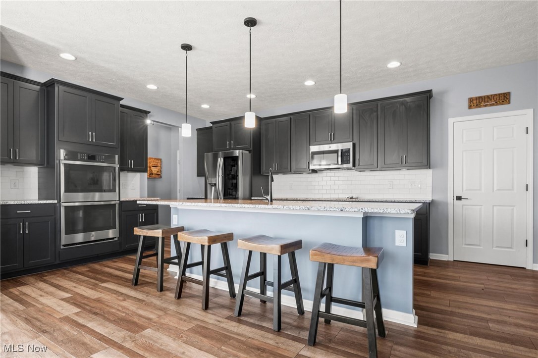37174 Amber Way North Ridgeville, OH 44039 - Photo 2 of 40 Kitchen with appliances with stainless steel finishes, wood finished floors, a center island with sink, backsplash, and a kitchen bar