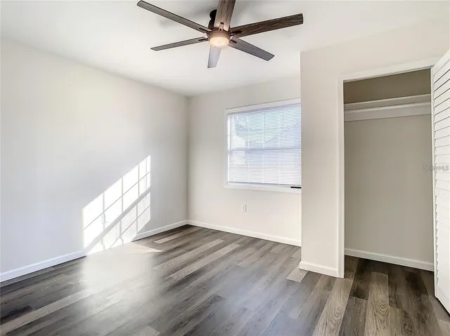 an empty room with wooden floor fan and windows
