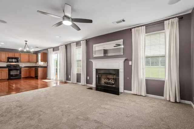 a view of a livingroom with a fireplace a ceiling fan and a kitchen view