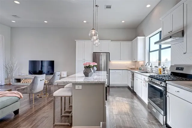 a kitchen with stainless steel appliances granite countertop a stove a sink dishwasher a refrigerator white cabinets and wooden floor