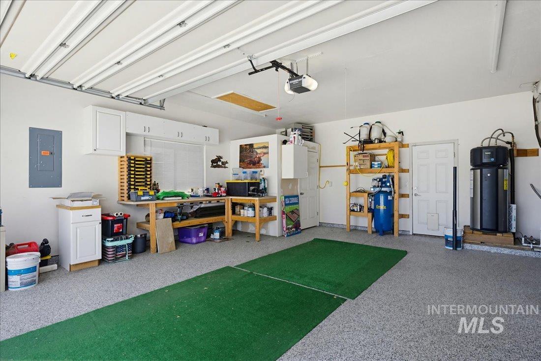 24623 Falcon Lane Caldwell, ID 83607 - Photo 23 of 40 Spacious garage featuring a speckled epoxy floor, extensive overhead fluorescent lighting, built-in cabinetry, a workbench, and a water heater system
