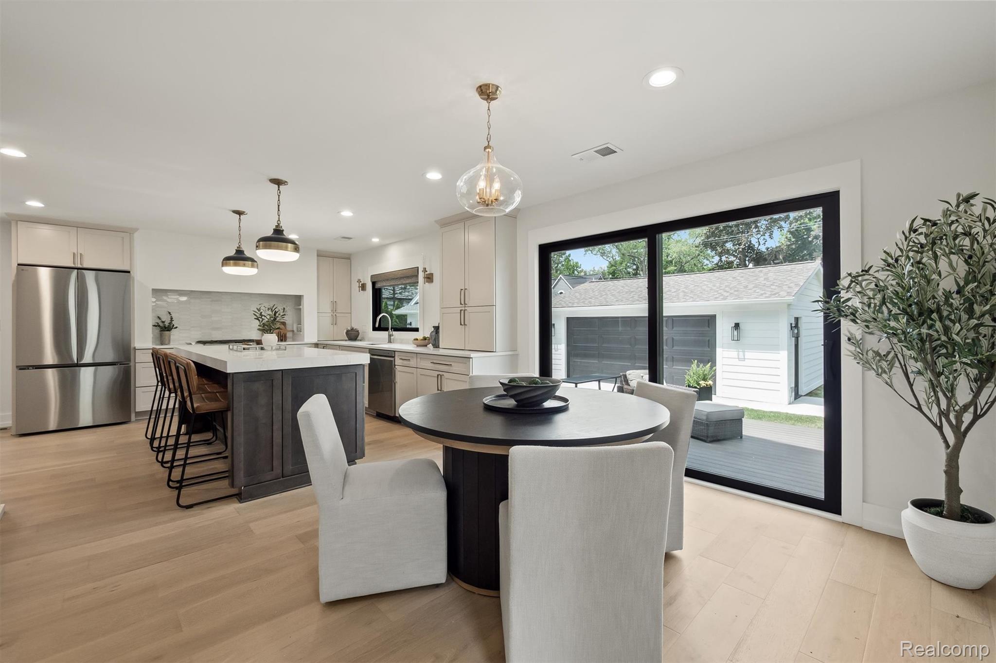 347 Highland Avenue Rochester, MI 48307 - Photo 18 of 59 Open-concept kitchen and dining area featuring light wood-finish flooring, a kitchen island with seating, stainless steel appliances, a tile backsplash, and a sliding glass door to an outdoor deck