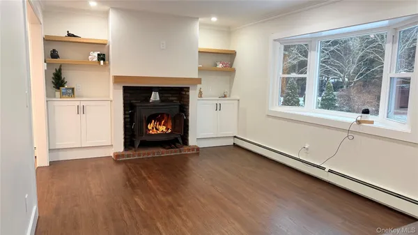 a view of an empty room with wooden floor fireplace and a window