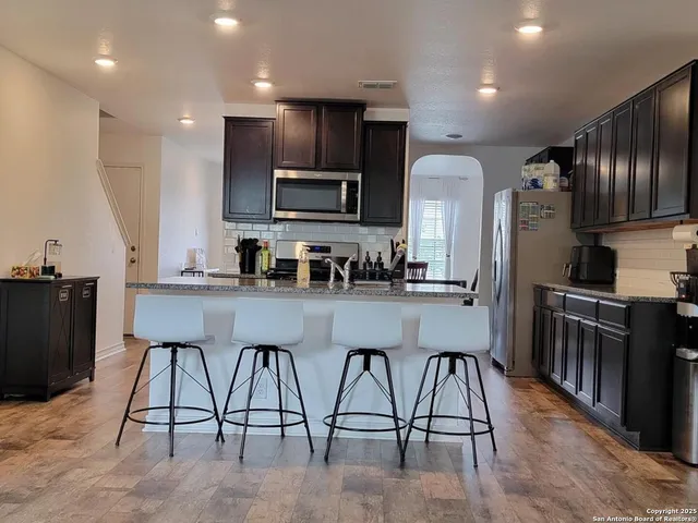 a kitchen with stainless steel appliances kitchen island granite countertop a refrigerator a stove a sink a dining table and chairs with wooden floor