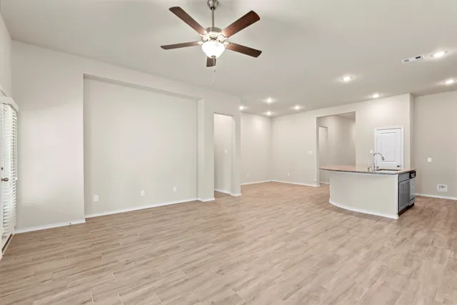 a view of an empty room and kitchen with ceiling fan