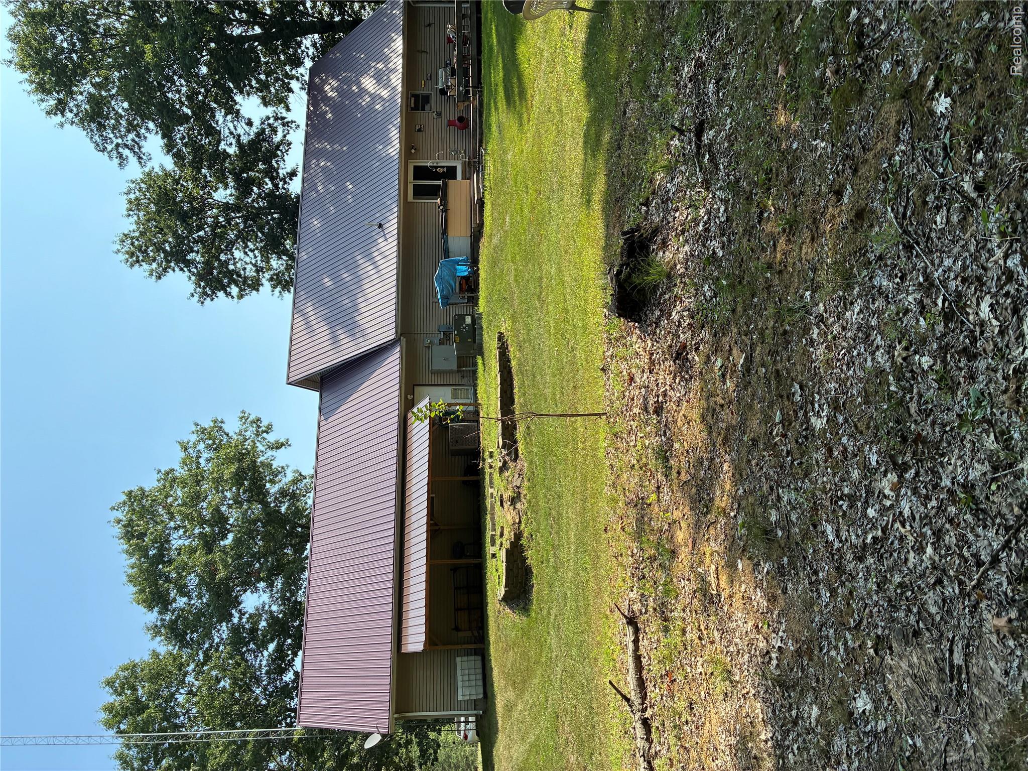 10995 East Isabella County Line Road Coleman, MI 48618 - Photo 75 of 76 Two-story residence with a metal roof, an expansive covered patio, and a spacious backyard featuring mature trees