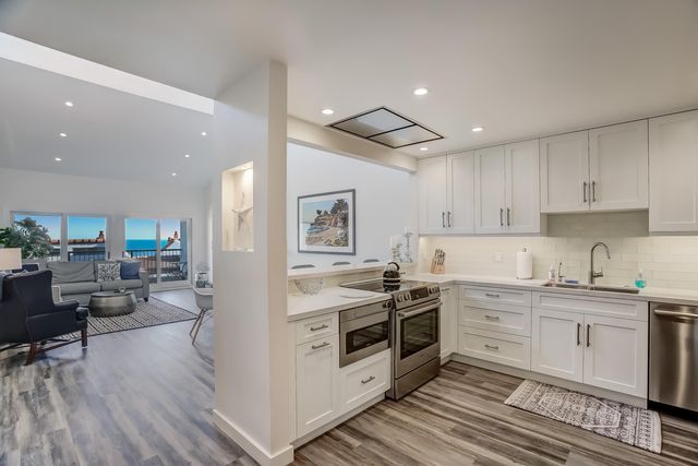 a kitchen with stainless steel appliances a stove top oven a sink a refrigerator and white cabinets with wooden floor