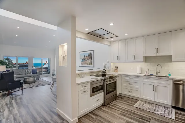 a kitchen with stainless steel appliances a stove top oven a sink a refrigerator and white cabinets with wooden floor