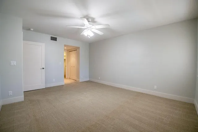 an empty room with a chandelier fan and windows