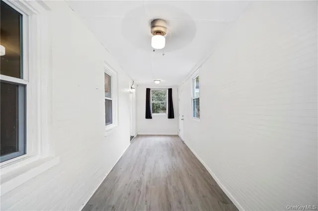 an empty room with wooden floor chandelier fan and windows