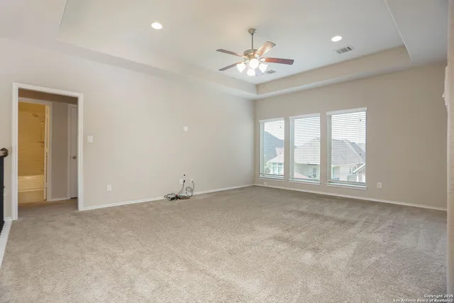 an empty room with chandelier fan and windows
