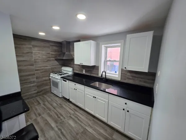 a kitchen with granite countertop a sink a stove cabinets and wooden floor