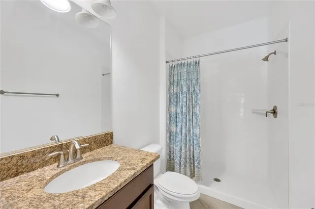 a bathroom with a granite countertop sink a toilet a mirror and shower