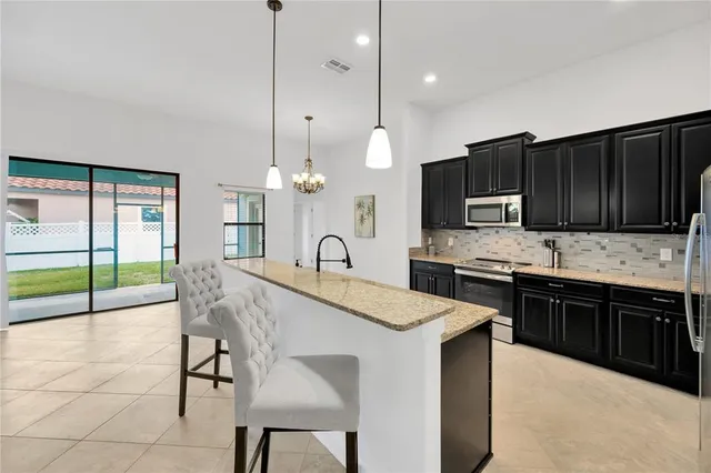 a kitchen with stainless steel appliances kitchen island granite countertop a table chairs sink and stove top oven