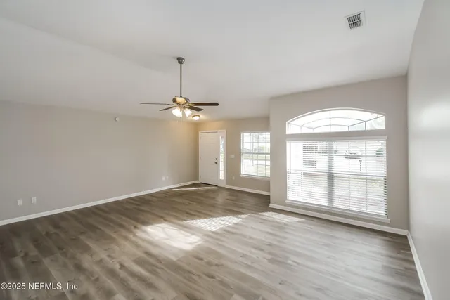 an empty room with wooden floor chandelier and windows