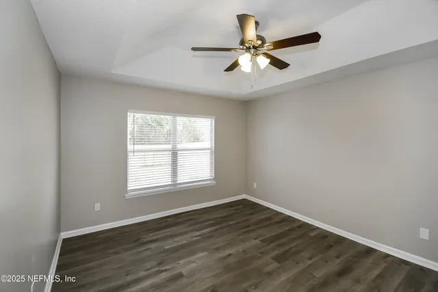 an empty room with wooden floor fan and windows