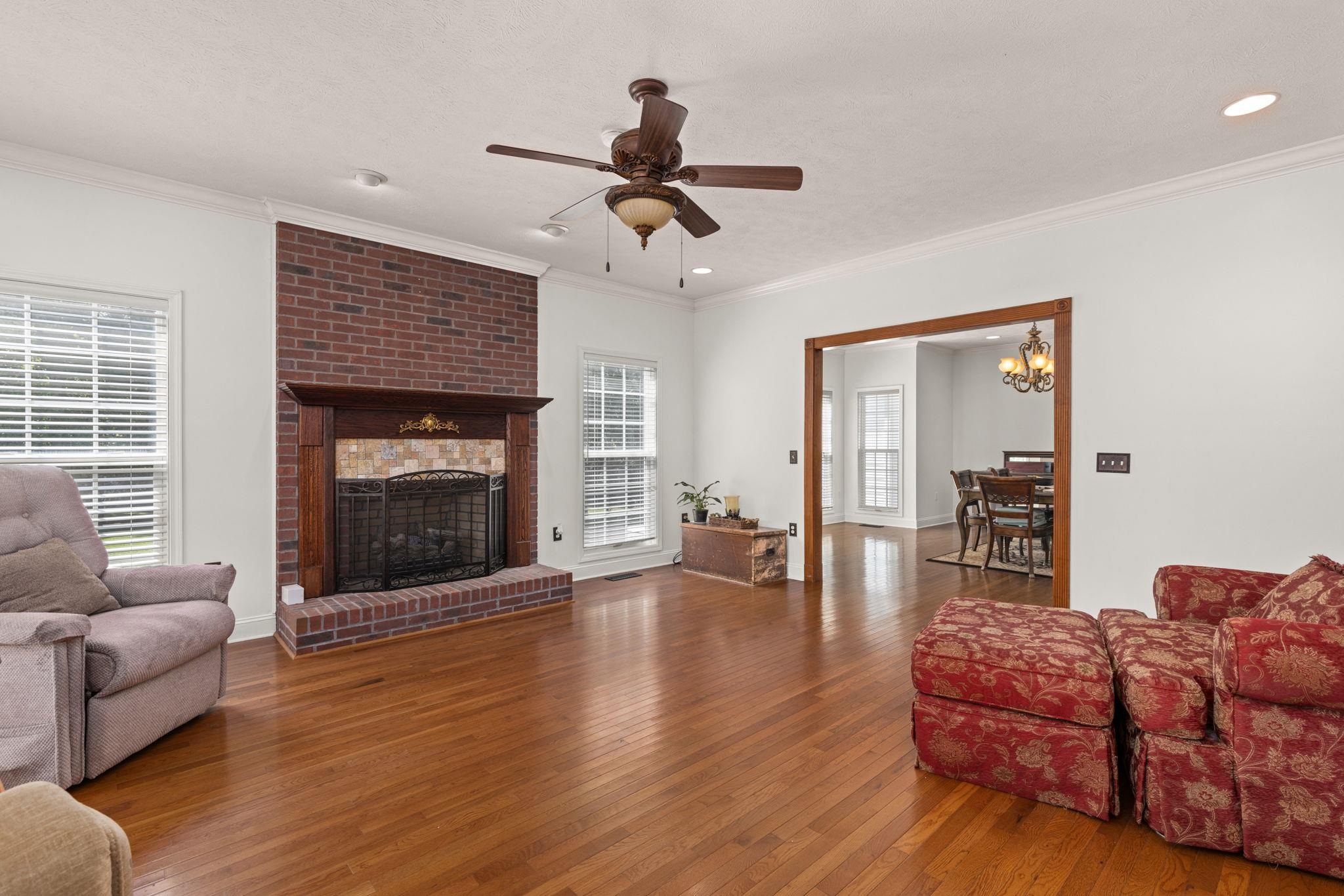20 Tadpole Lane Corinth, MS 38834 - Photo 30 of 38 Living area featuring wood-type flooring, ornamental molding, a brick fireplace, ceiling fan, and a chandelier
