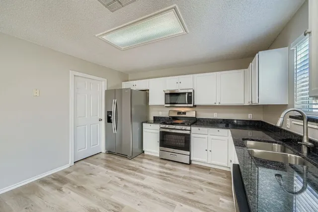 a kitchen with granite countertop a refrigerator a sink dishwasher a stove and white cabinets with wooden floor