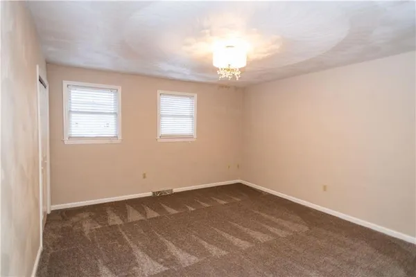 an empty room with a chandelier fan and windows