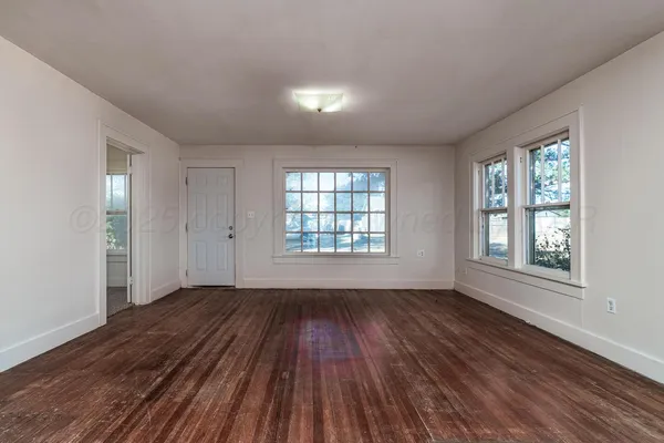 a view of an empty room with wooden floor and a window