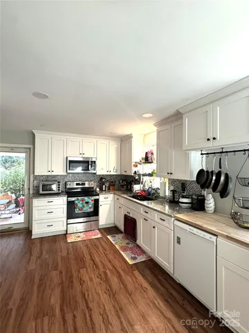 a kitchen with stainless steel appliances white cabinets a sink a stove a microwave and wooden floors