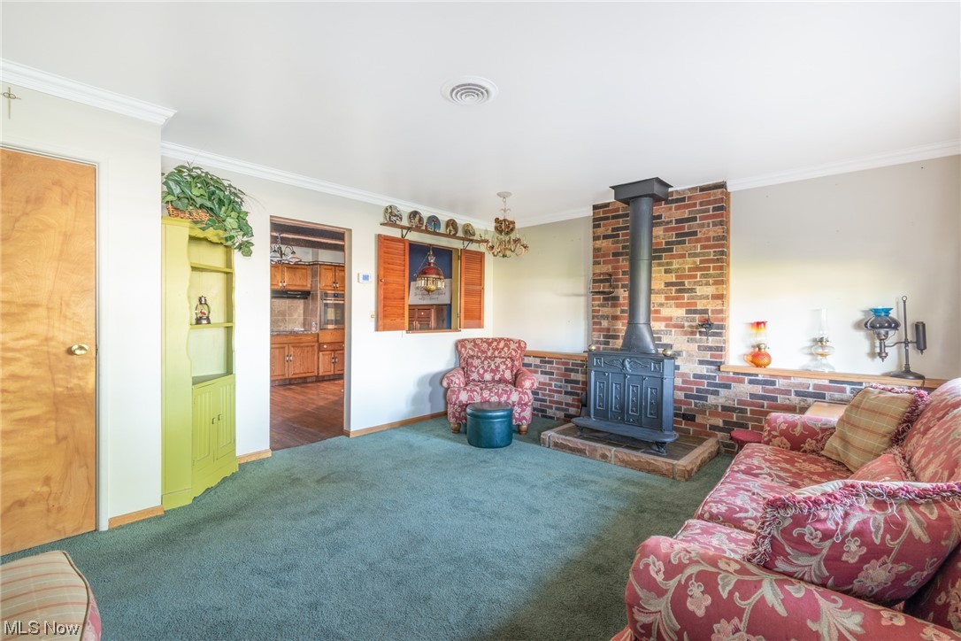 Carpeted living room with a fireplace, brick wall, and crown molding