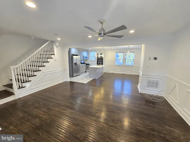 a view of a livingroom with wooden floor a ceiling fan and staircase